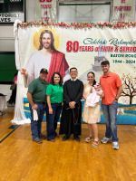 Five people pose on a gym floor in front of an “80 years” celebration banner and portrait backdrop.
