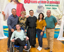 Group posing in front of a church anniversary banner; one person sits in a wheelchair.