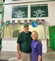 Two people standing in a school lobby beneath signboards, smiling and posing for a photo
