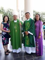 Four people posing outdoors, three in green religious vestments and one in a purple dress