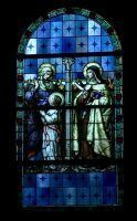 Stained glass of two robed figures beneath a blue arched window, one holding a small object.