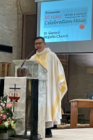 Priest in white and gold vestments speaking at a church lectern during Mass