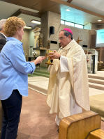 Clergy in white vestments greets a person in a blue blazer inside a church sanctuary