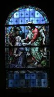 Stained-glass scene of a red-robed figure helping a person, set against a blue patterned background.