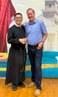 Two men smiling and posing together indoors, one in a black robe and the other in a blue shirt.