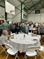 Group of people standing in a gym beside a round table set with plates and glasses