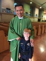 Man in green robe with a child in a dark outfit, standing together inside a church or chapel.