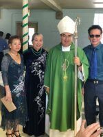 Four people posing outdoors, including a person in green clerical robes and mitre holding a staff.