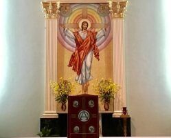 Church altar with a large Jesus mural, red lectern, and yellow flowers