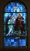 Stained-glass window with two haloed figures in robes, one in white and one in red, under a cross-shaped top panel