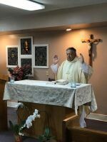 Priest standing at an altar during a church service, with a crucifix and flowers in the background