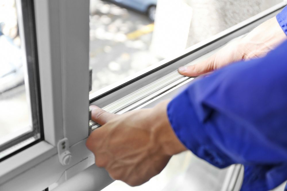 A Man In A Blue Jacket Is Fixing A Window — Ace Glass & Aluminium In Iluka, NSW