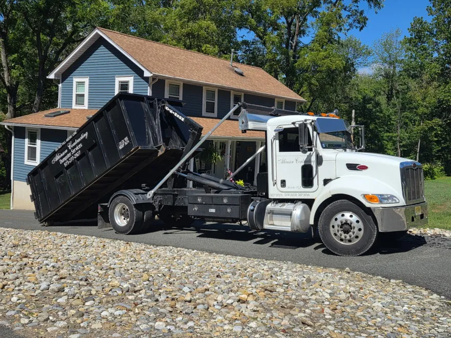 A green dumpster is sitting on top of a gravel road.