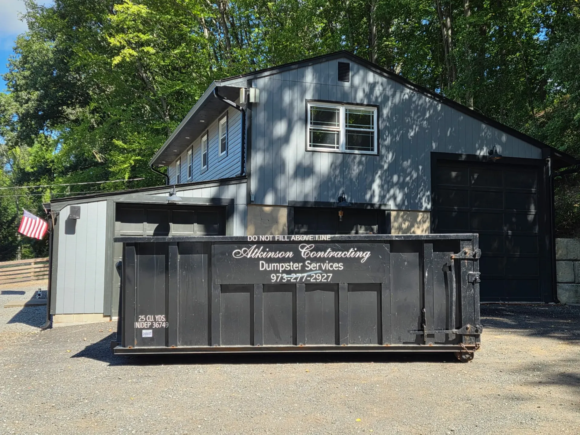 A green dumpster is parked in front of a house.