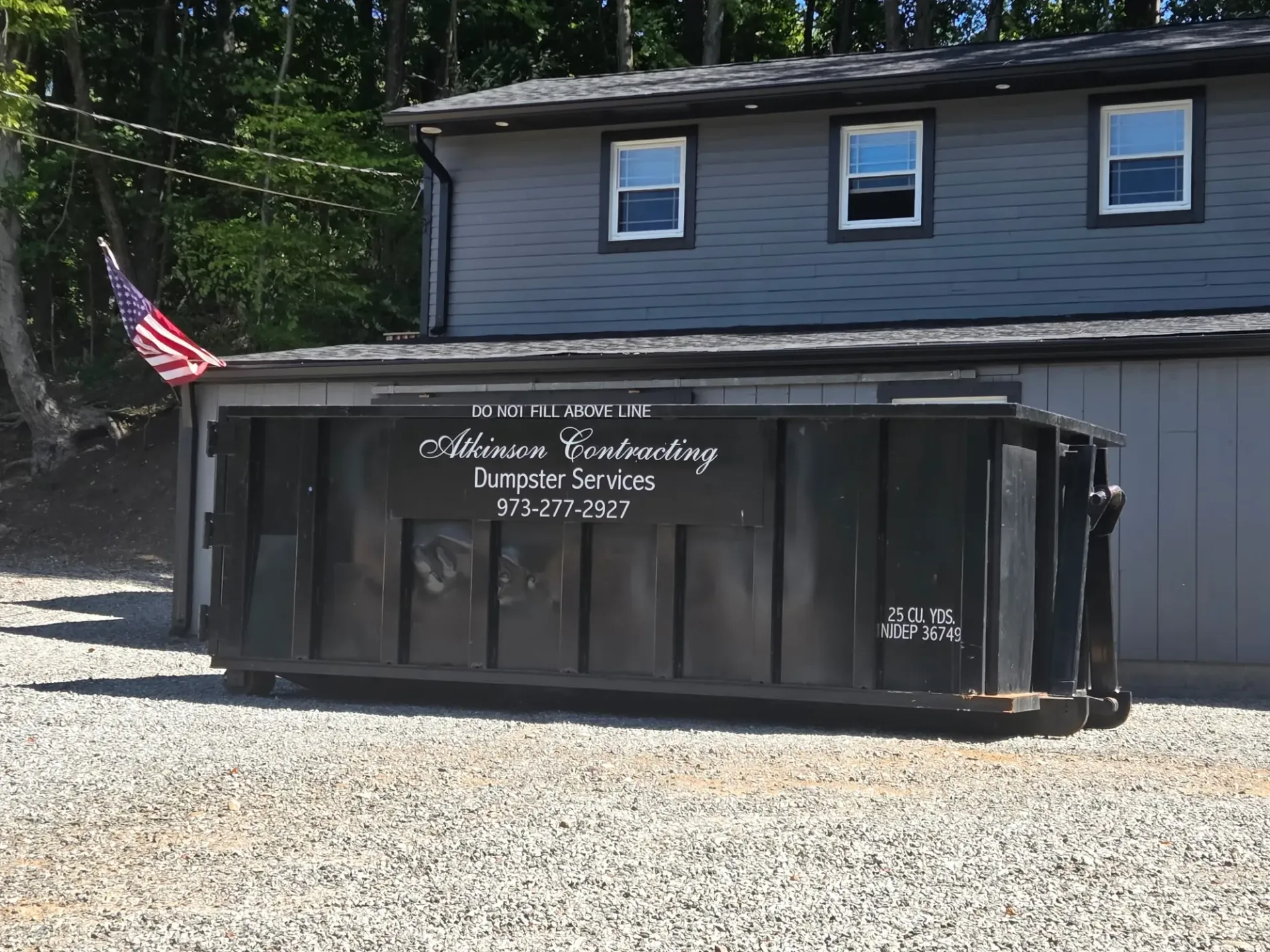 A row of dumpsters are parked in a gravel lot.