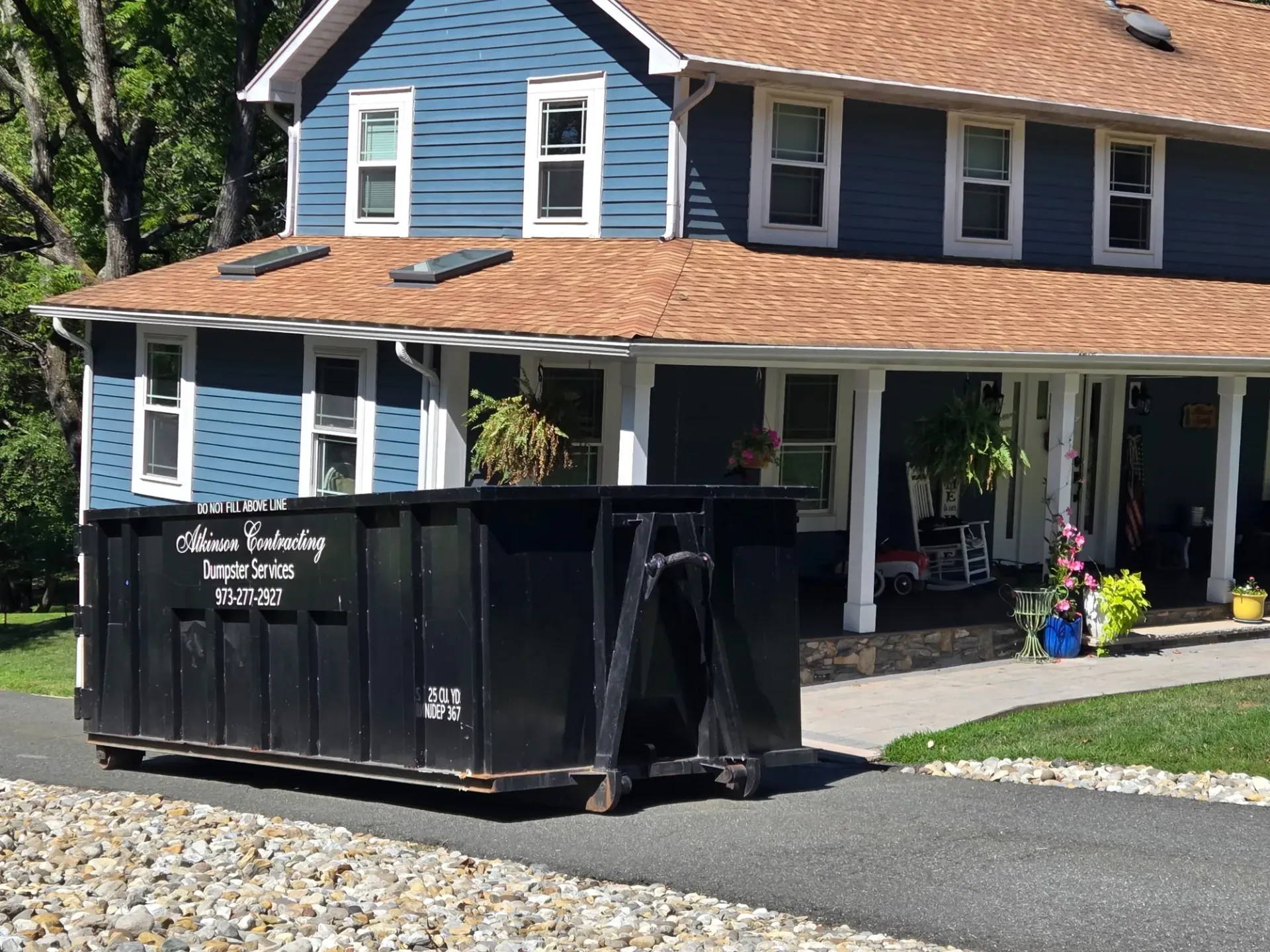 A green dumpster is parked in front of a house.