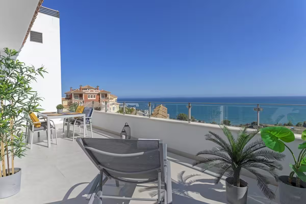 Modern seaside terrace with lounge chairs, potted plants, and ocean view under a blue sky