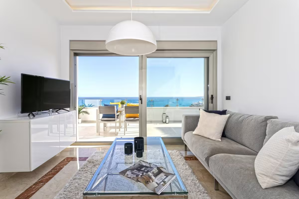 Bright living room with gray sofa, glass coffee table, TV, and ocean-view balcony doors