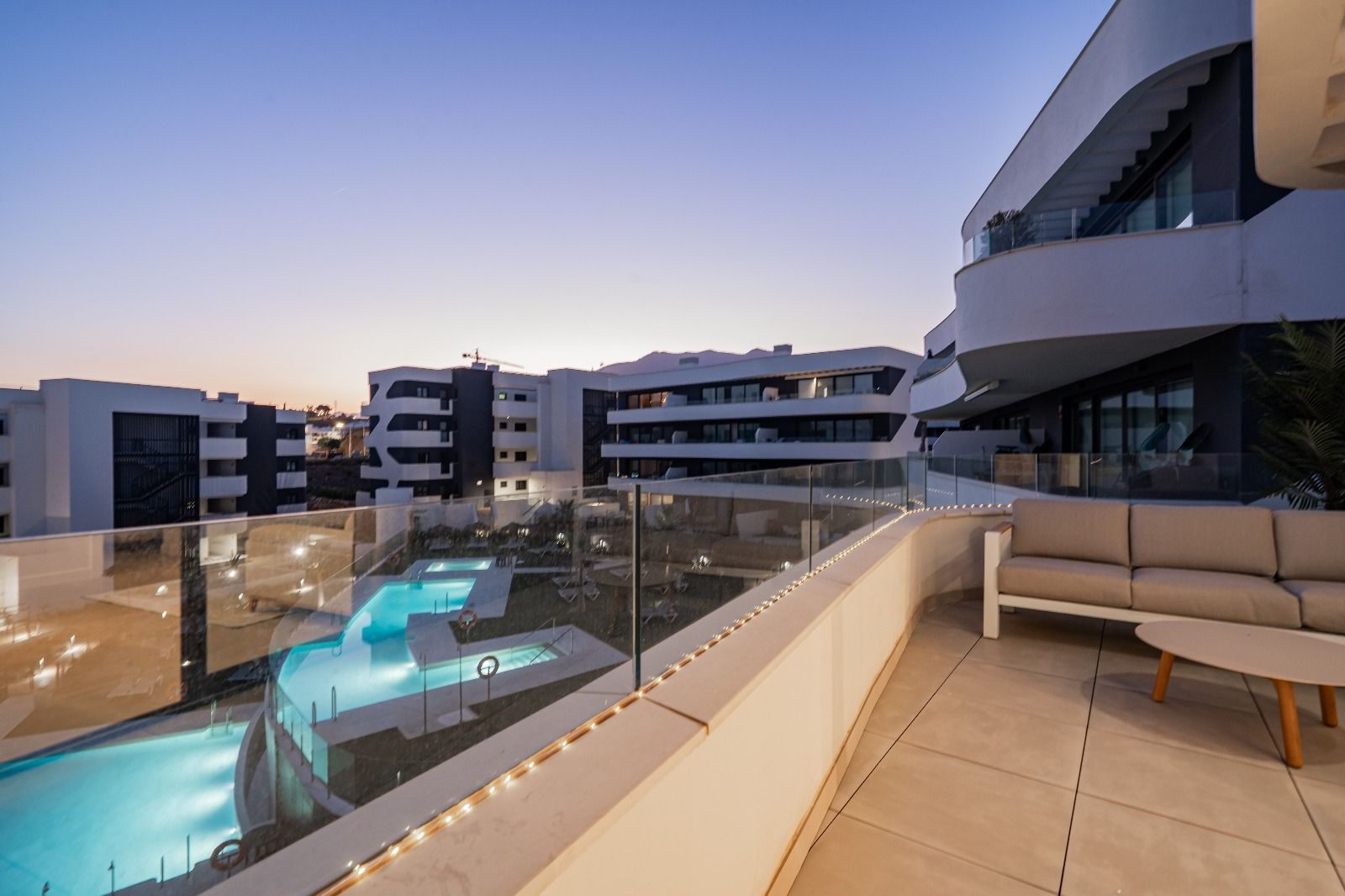 Balcony overlooking a modern apartment complex and lit pool at dusk