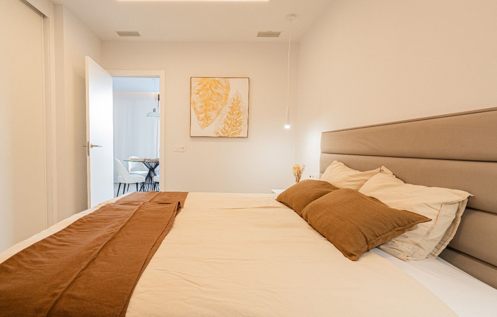 Bright bedroom with a large bed, beige headboard, and open doorway to a bathroom or vanity area