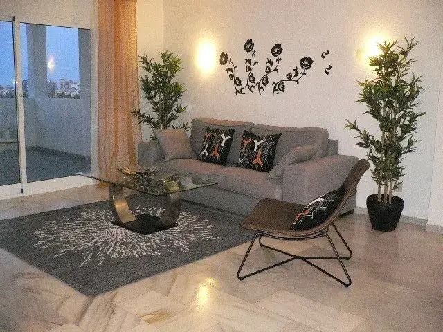 Modern living room with gray sofa, lounge chair, coffee table, plants, and sliding glass doors.