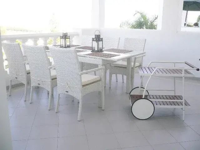 Bright white patio dining area with table, chairs, lanterns, and a wheeled serving cart.