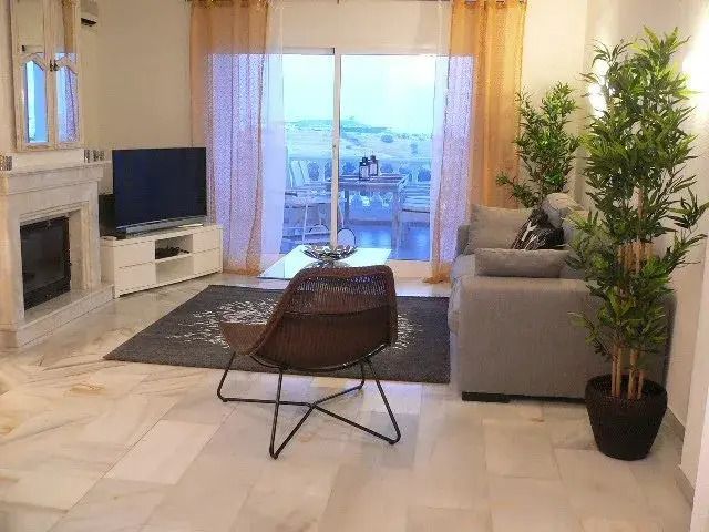 Modern living room with sofa, chair, TV, fireplace, and sliding doors to a balcony view