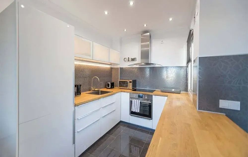 Modern white kitchen with wooden countertops, built-in oven, and gray backsplash