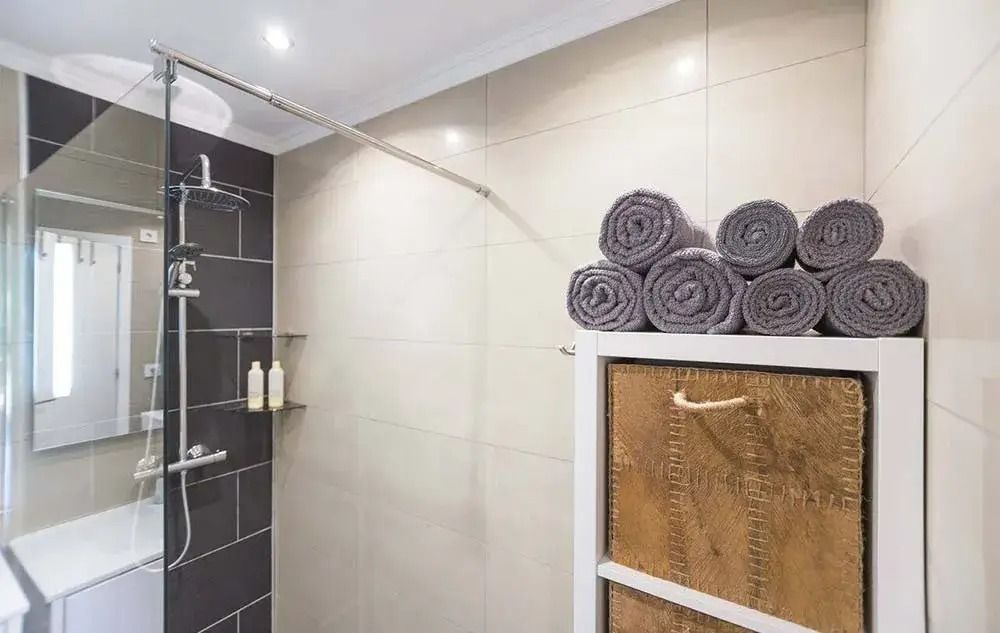 Modern bathroom with tiled shower, glass enclosure, and stacked gray towels on a cabinet