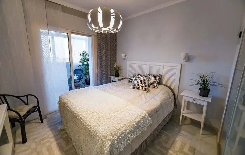 Bright bedroom with a bed, chandelier, side tables, chair, and balcony doors