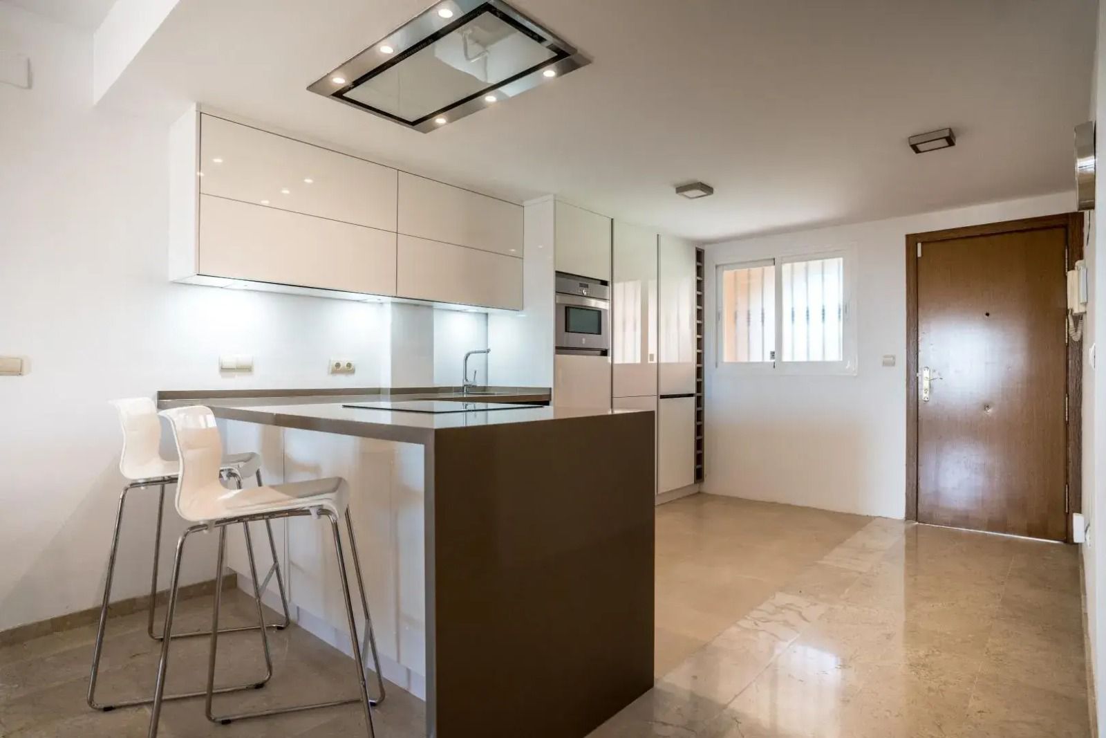 Modern kitchen with island seating, white cabinets, and a stainless-steel refrigerator near an entry door.