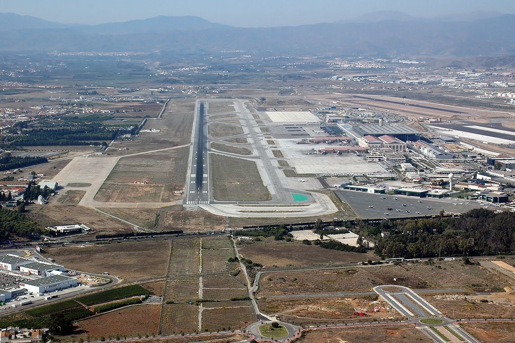 Aerial view of a long airport runway with terminal buildings and mountains in the distance.