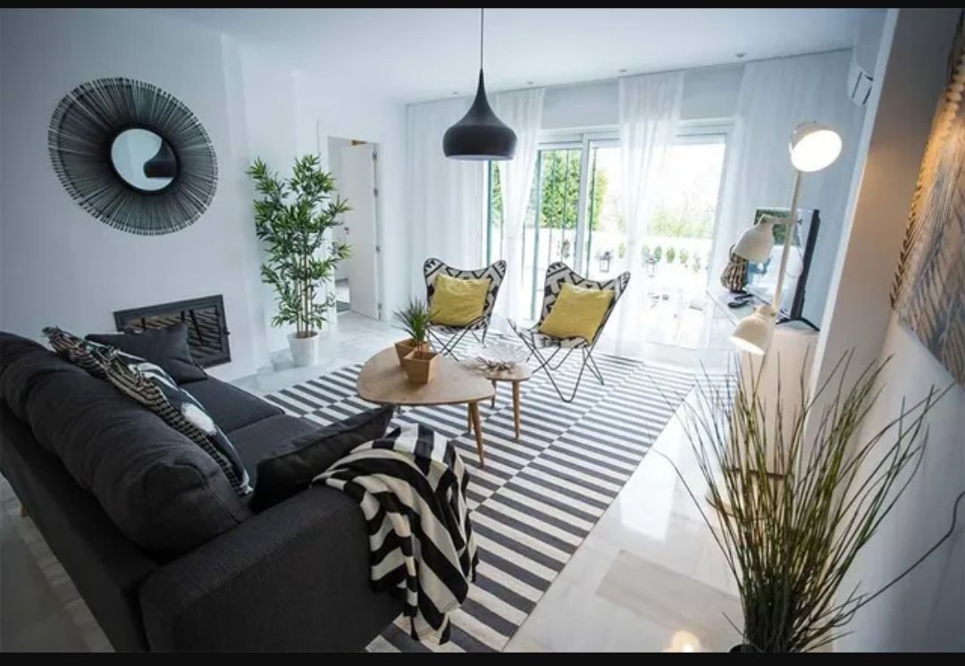 Modern living room with black sofa, striped rug, yellow chairs, and bright windows