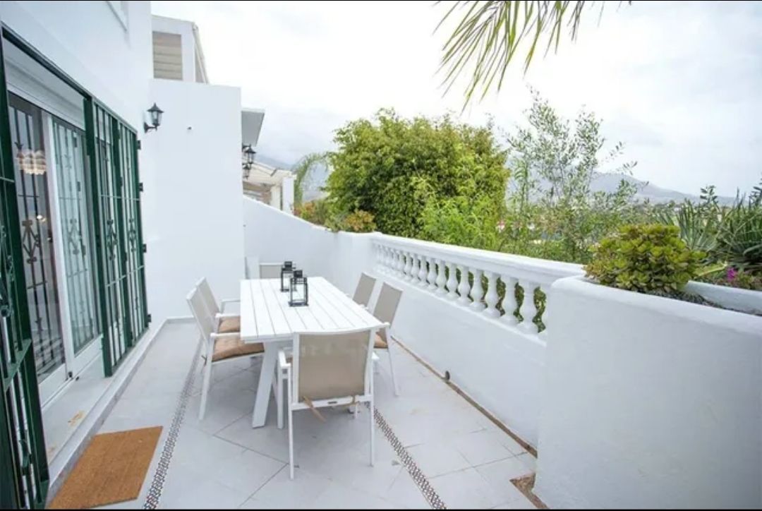 White patio with dining table, chairs, and greenery along a modern balcony terrace.