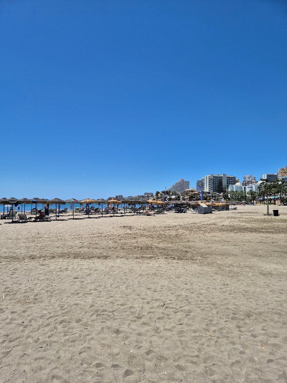 Coastal resort with apartment buildings, sandy beach, blue sea, and a long pier over green water