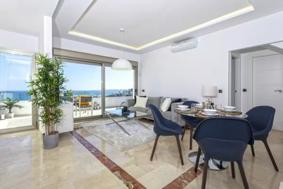 Bright modern living-dining room with blue chairs, marble floor, and ocean-view balcony