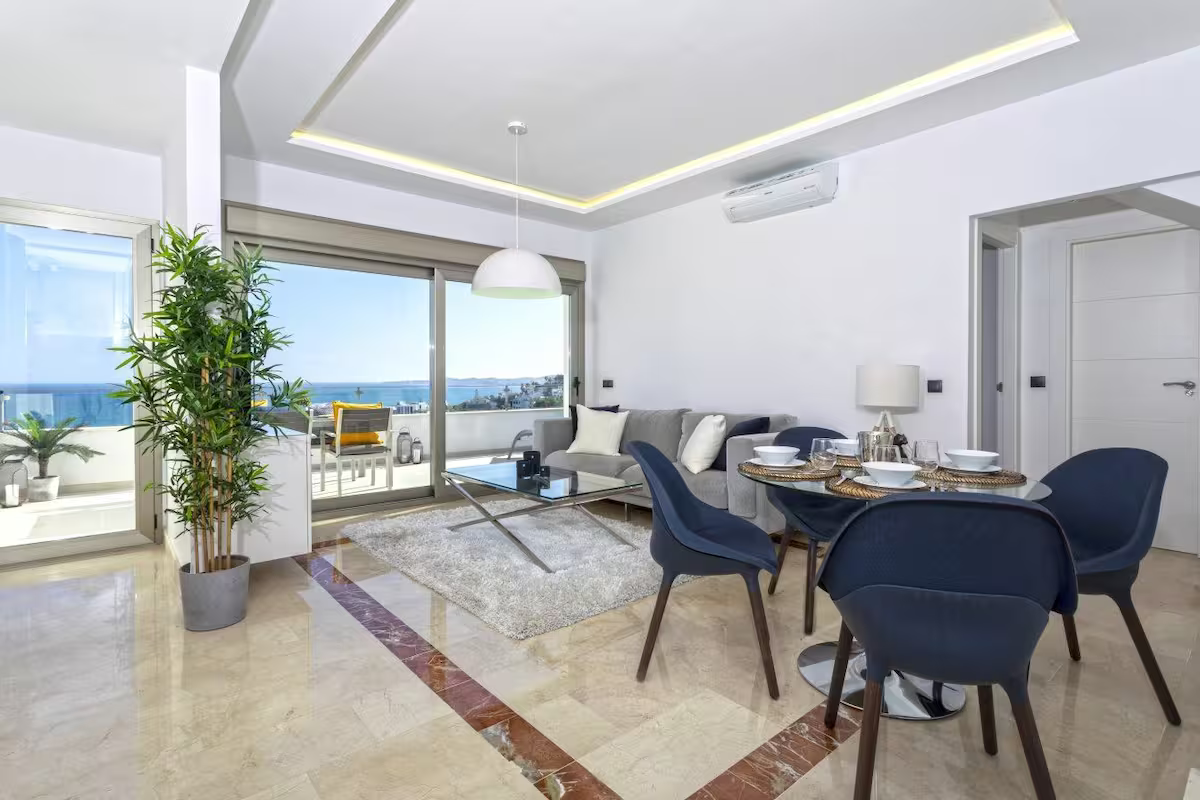 Bright modern dining room with blue chairs, marble floor, and sliding doors to a balcony with ocean view