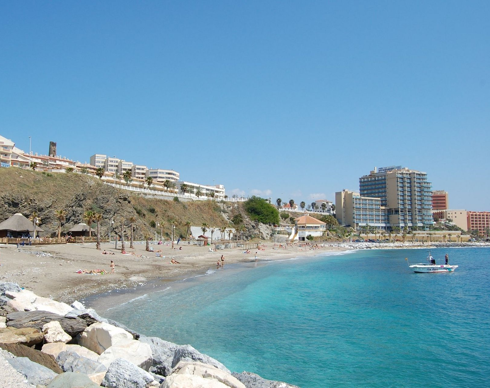 Coastal resort with apartment buildings, sandy beach, blue sea, and a long pier over green water