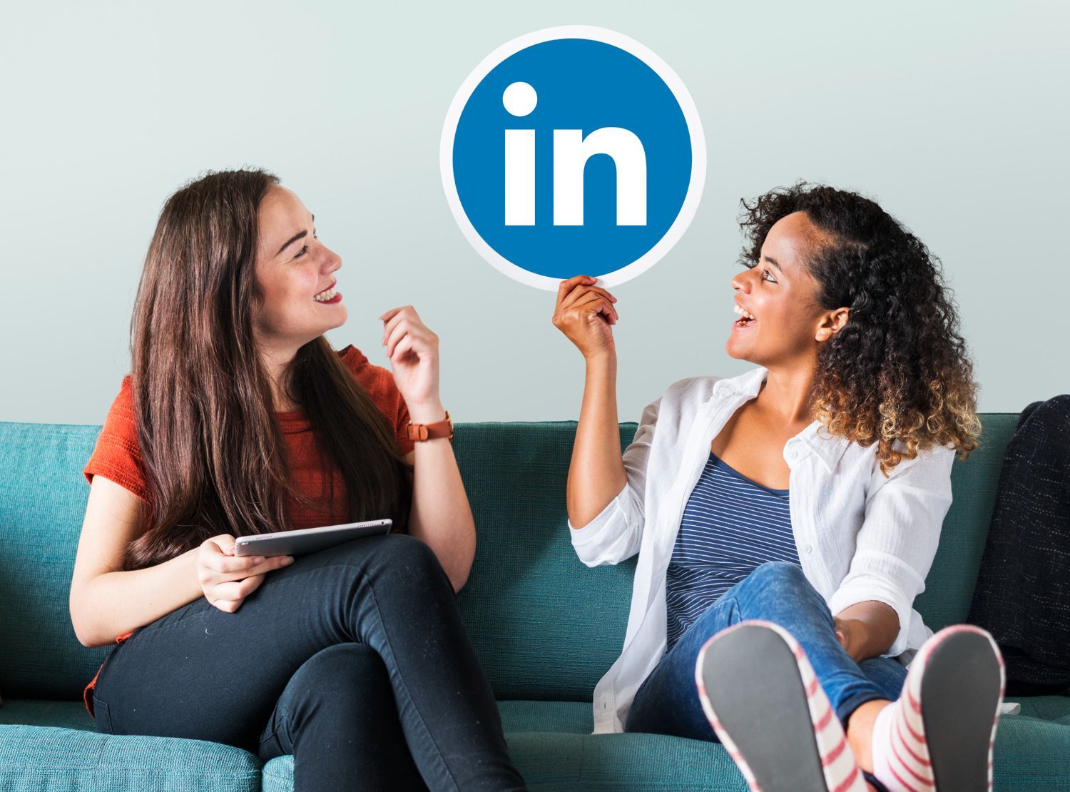 Two people sitting on a couch holding a LinkedIn logo sign and smiling at each other