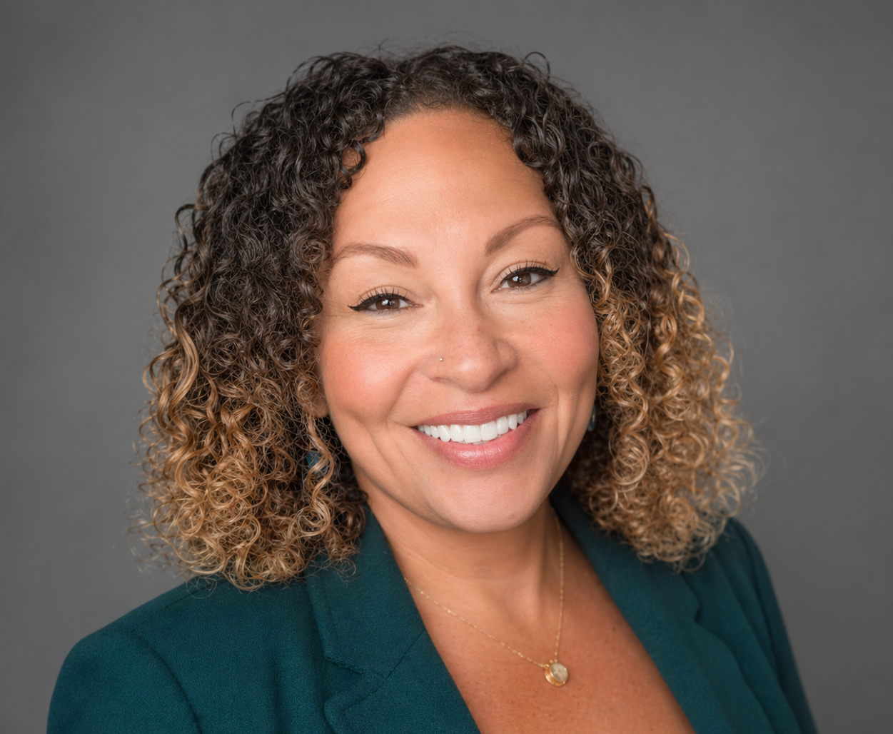 Smiling woman with curly hair in teal blazer on gray background