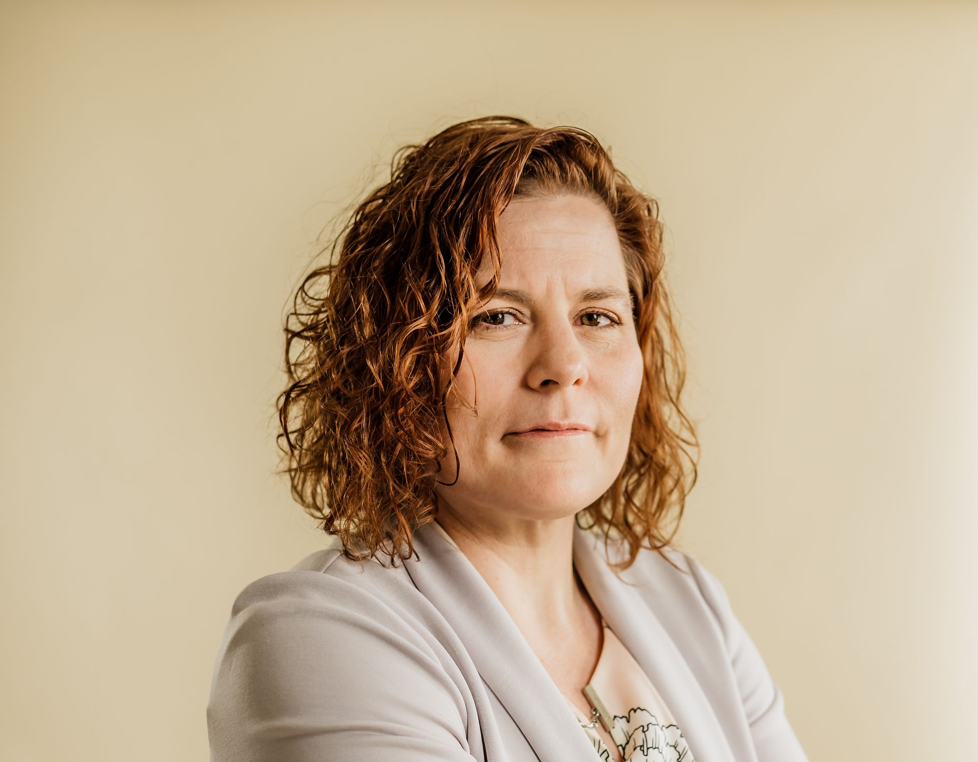 Portrait of a person with curly hair and a light cardigan against a beige background
