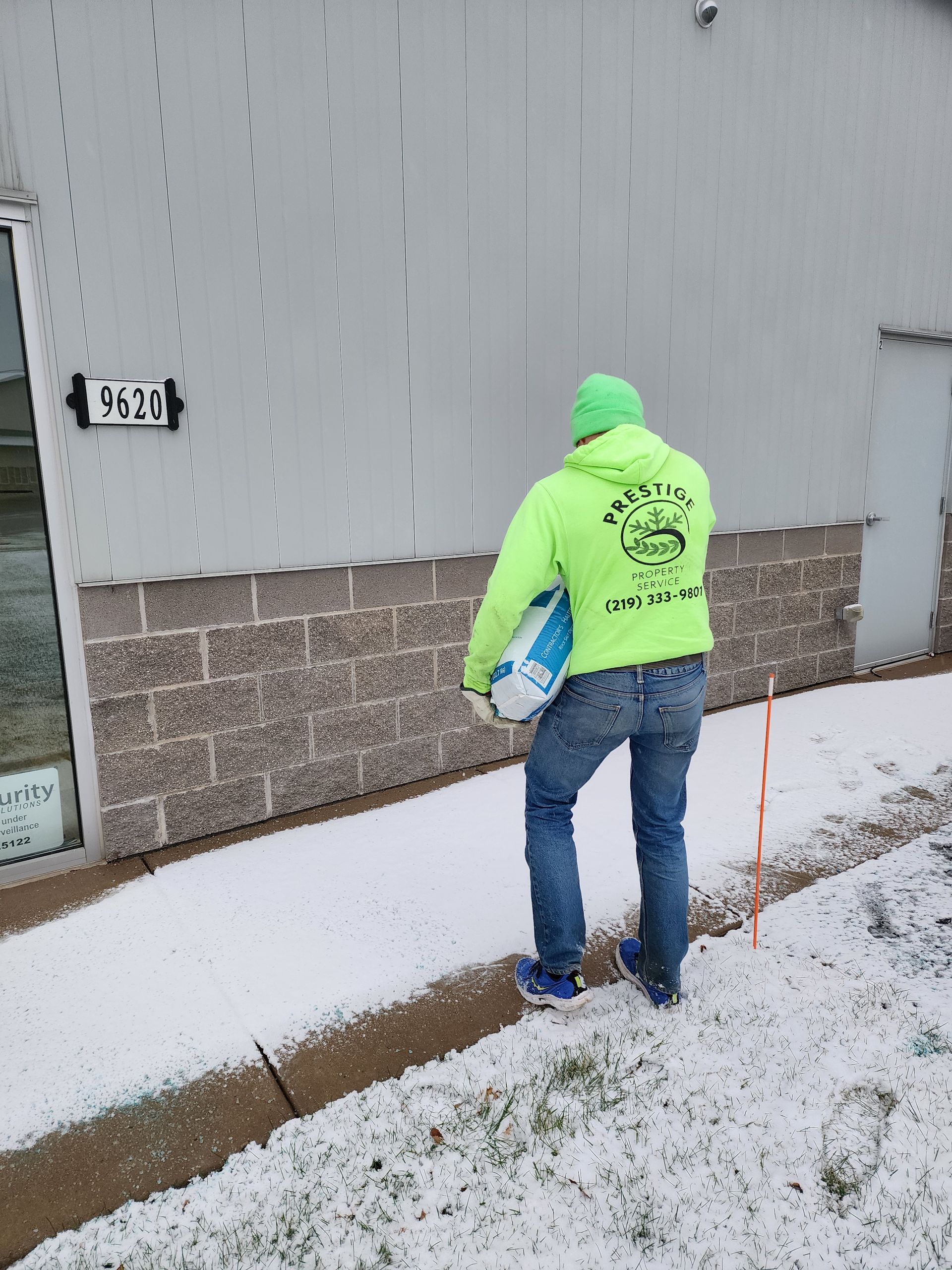 Person in neon green hoodie carrying a bag outside a building in snowy conditions