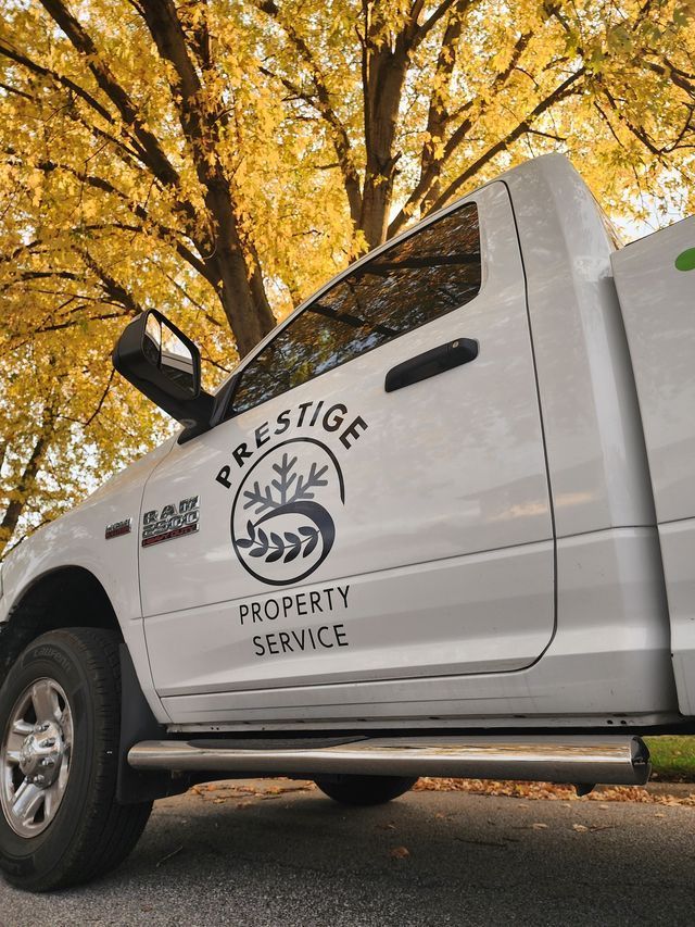 White Prestige Property Service truck parked under golden autumn trees