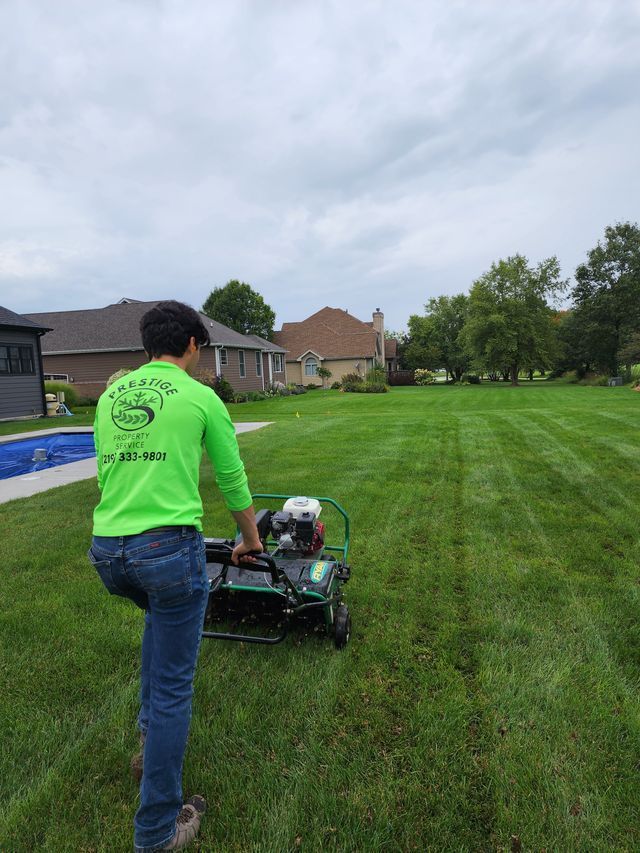 Person mowing a green lawn beside a house on an overcast day