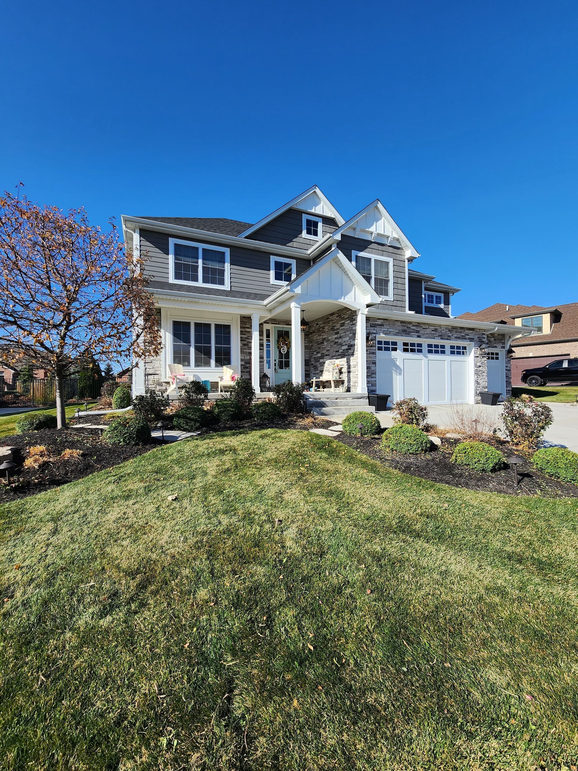 Large blue-and-white two-story house with a front porch, garage, and landscaped yard under a clear sky