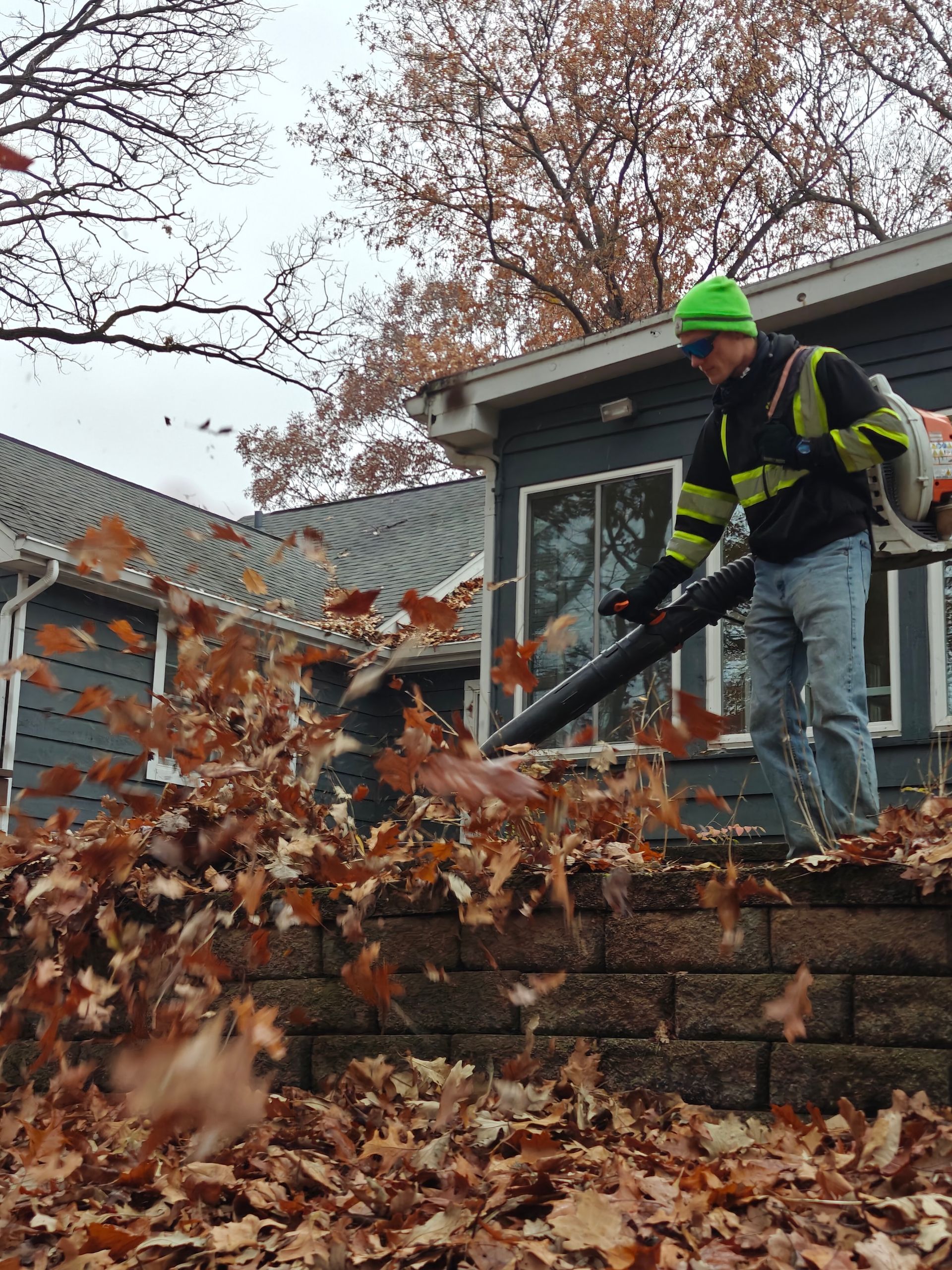 Worker in green helmet blowing leaves off a stone wall in a yard