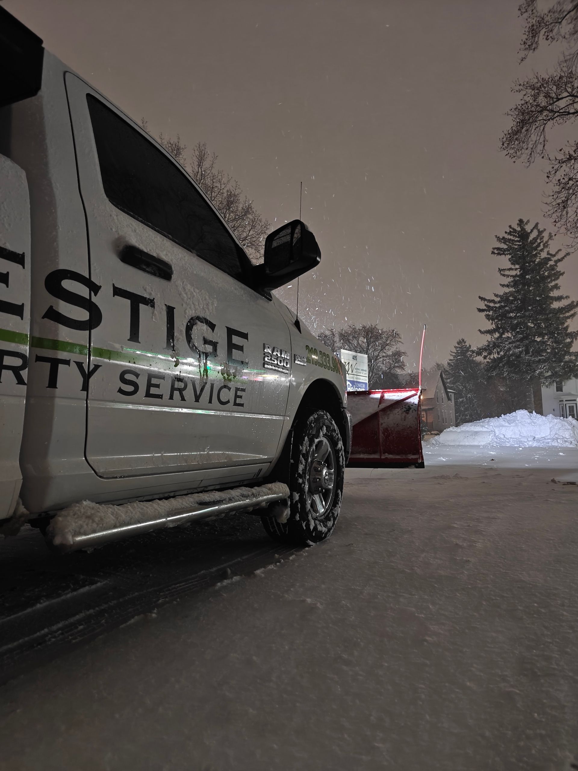 Snowy night beside a black Prestige Security truck and a red car on a road
