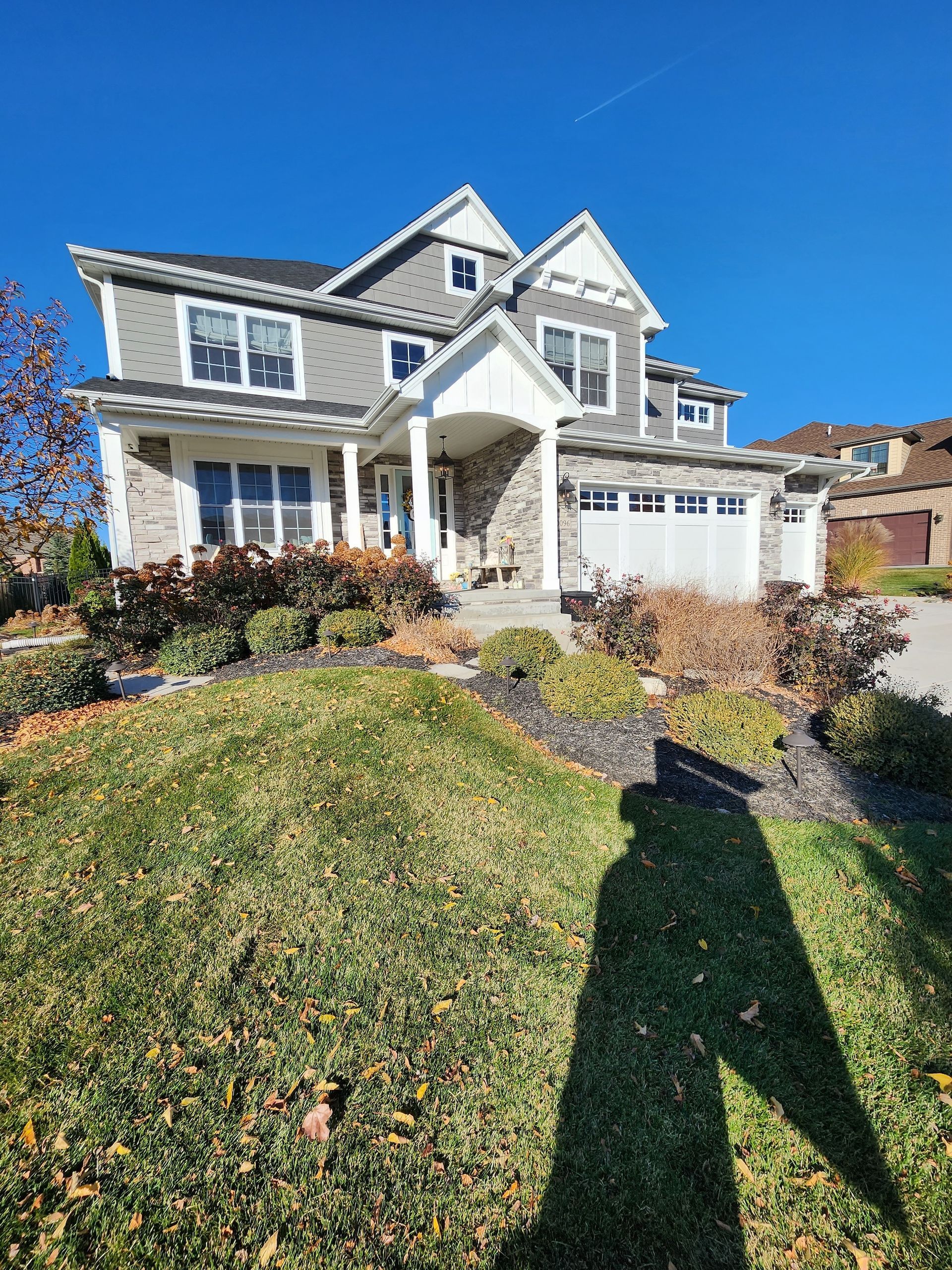 Suburban two-story house with stone facade, white trim, and a front lawn under a clear blue sky
