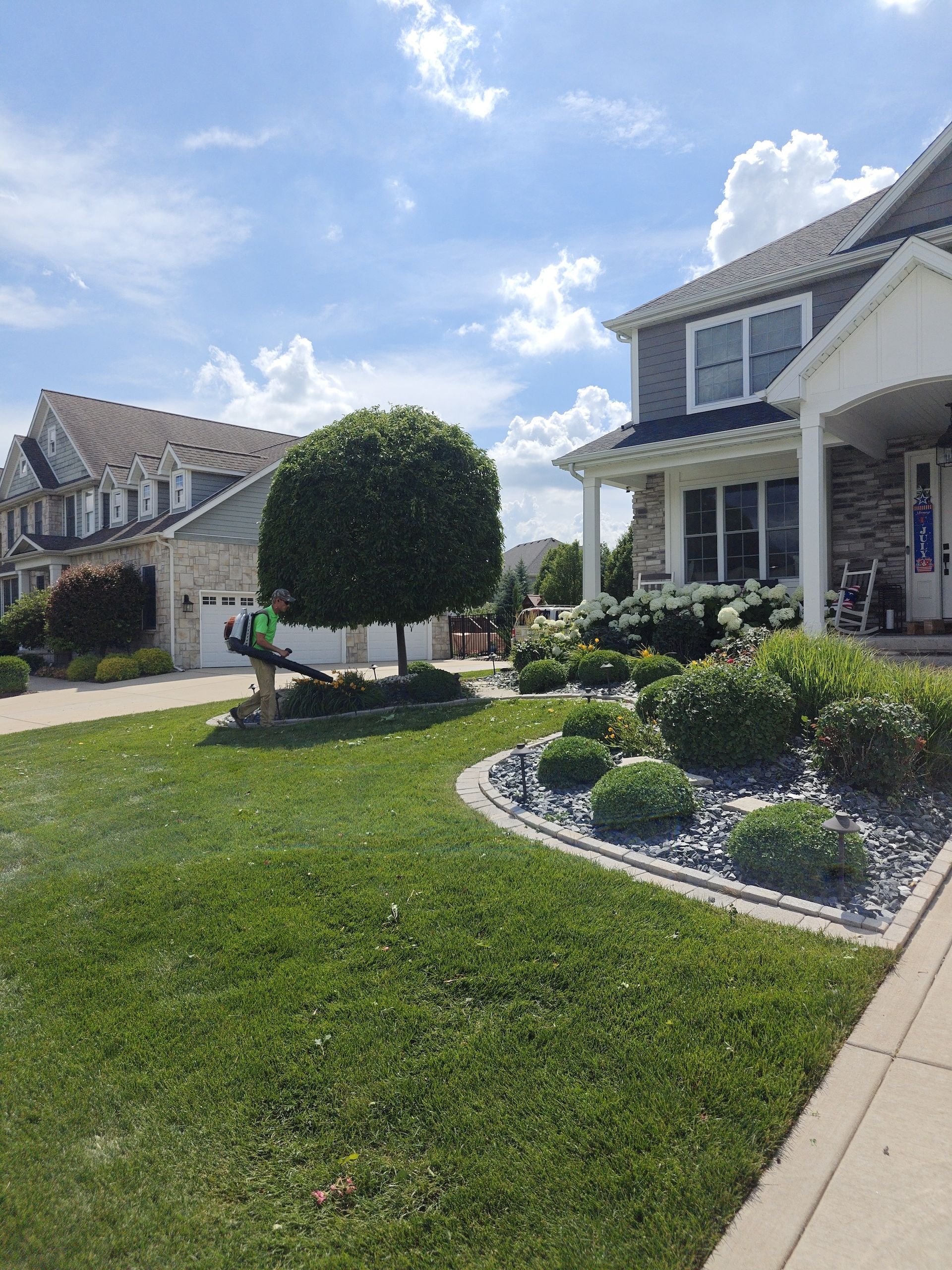 Suburban homes with manicured lawn, trimmed shrubs, and a blue sky with clouds