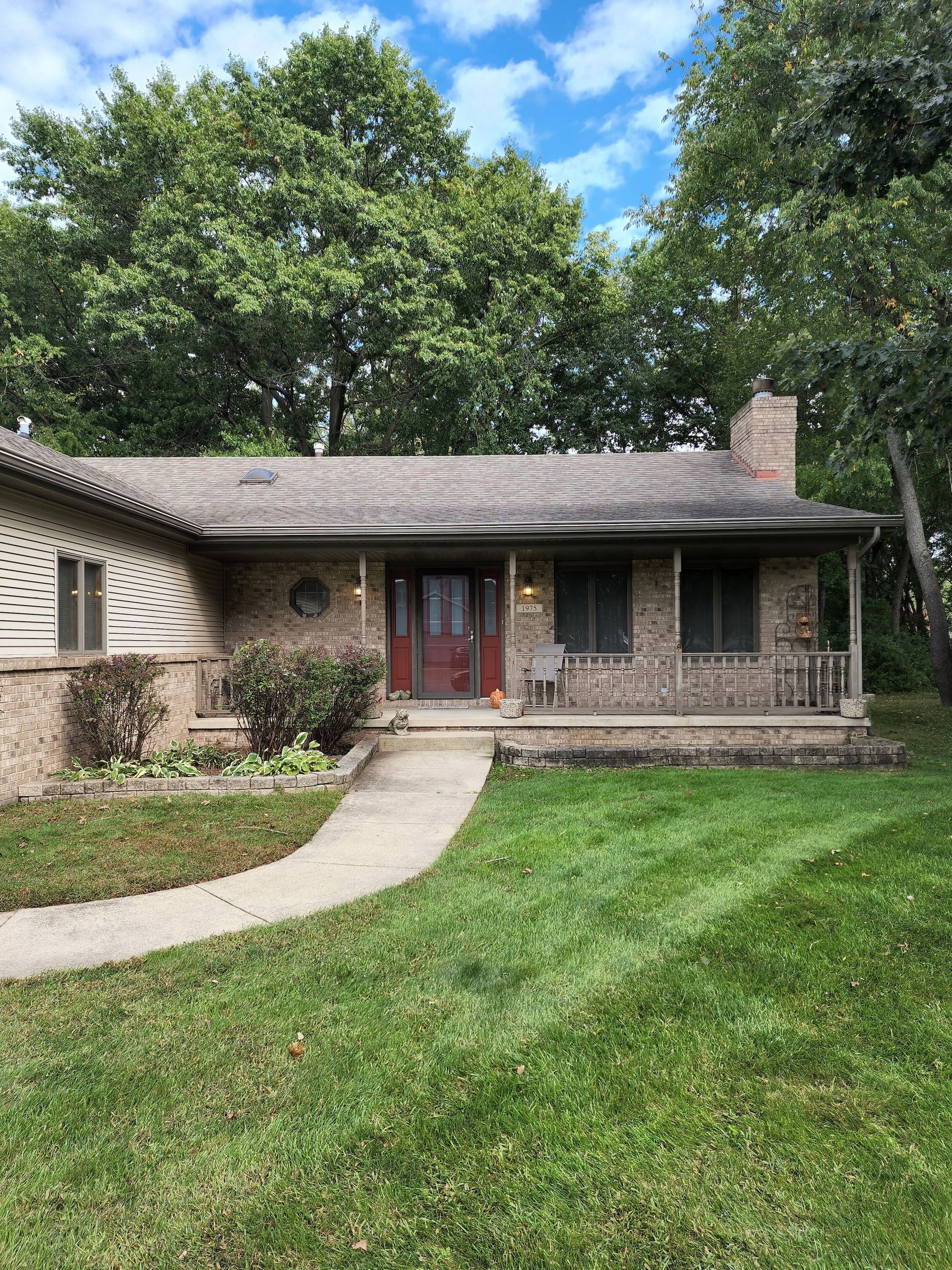 Single-story brick house with red front door, curved walkway, and green lawn under trees